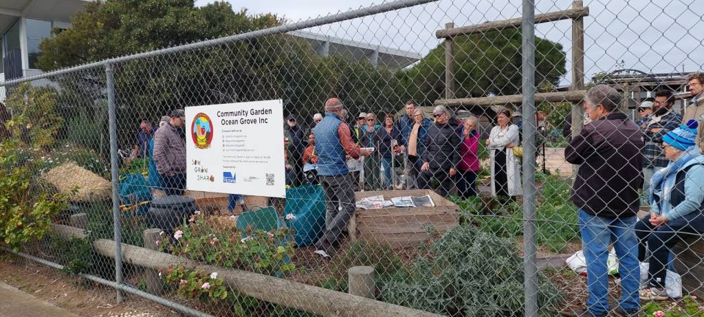 A group of people standing in the Community Garden paying attention to a man demonstrating gardening techniques